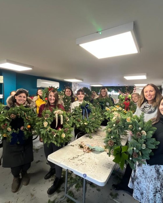 A group holding the Christmas wreaths they made at a private workshop