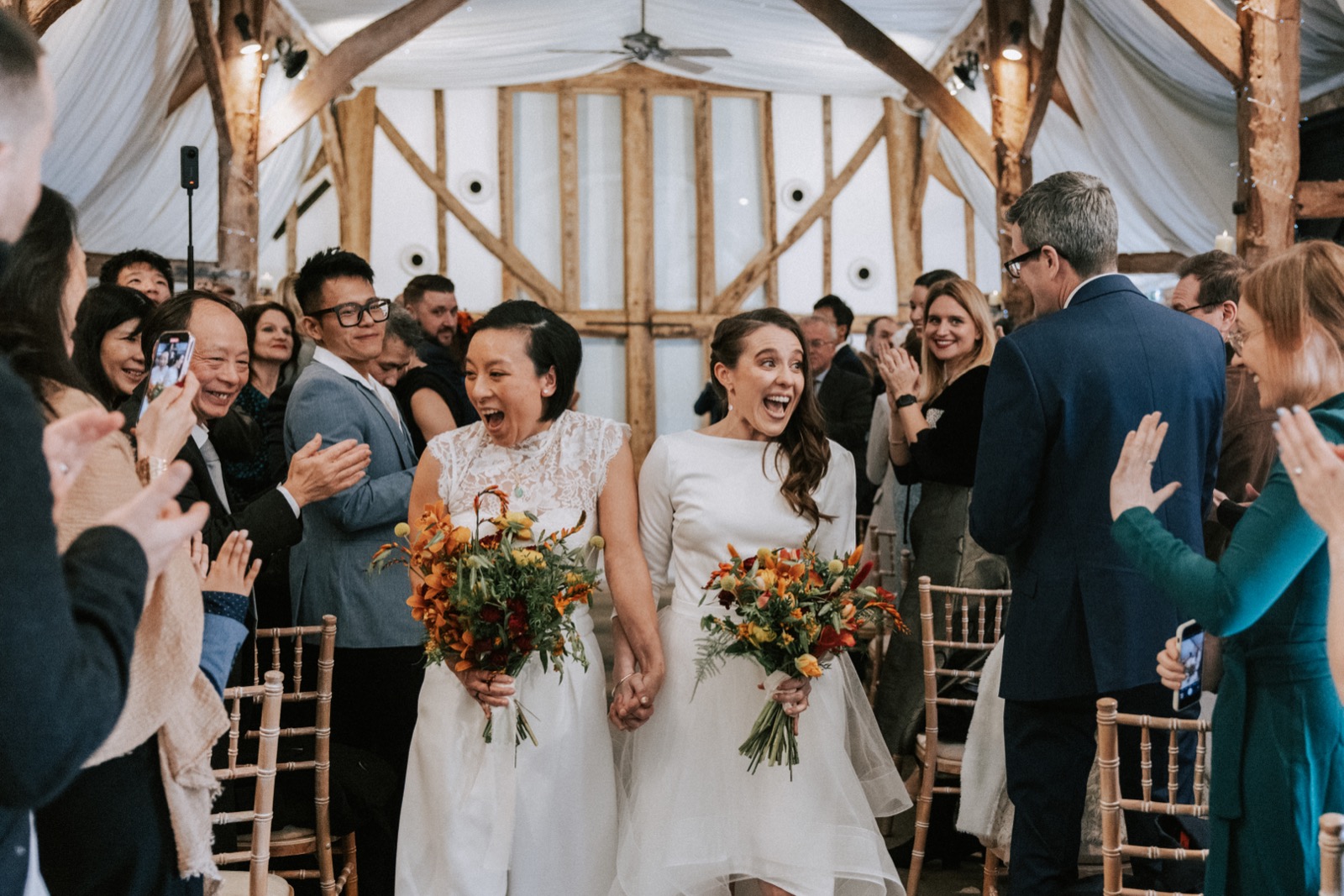Ruth and Hoi Ye walking back down the aisle at South Farm, carrying autumn bouquets by Gin House Flowers
